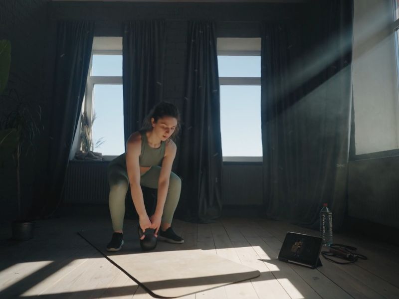 devojka trenira u kućnim uslovima koristeći bučicu i strunjaču